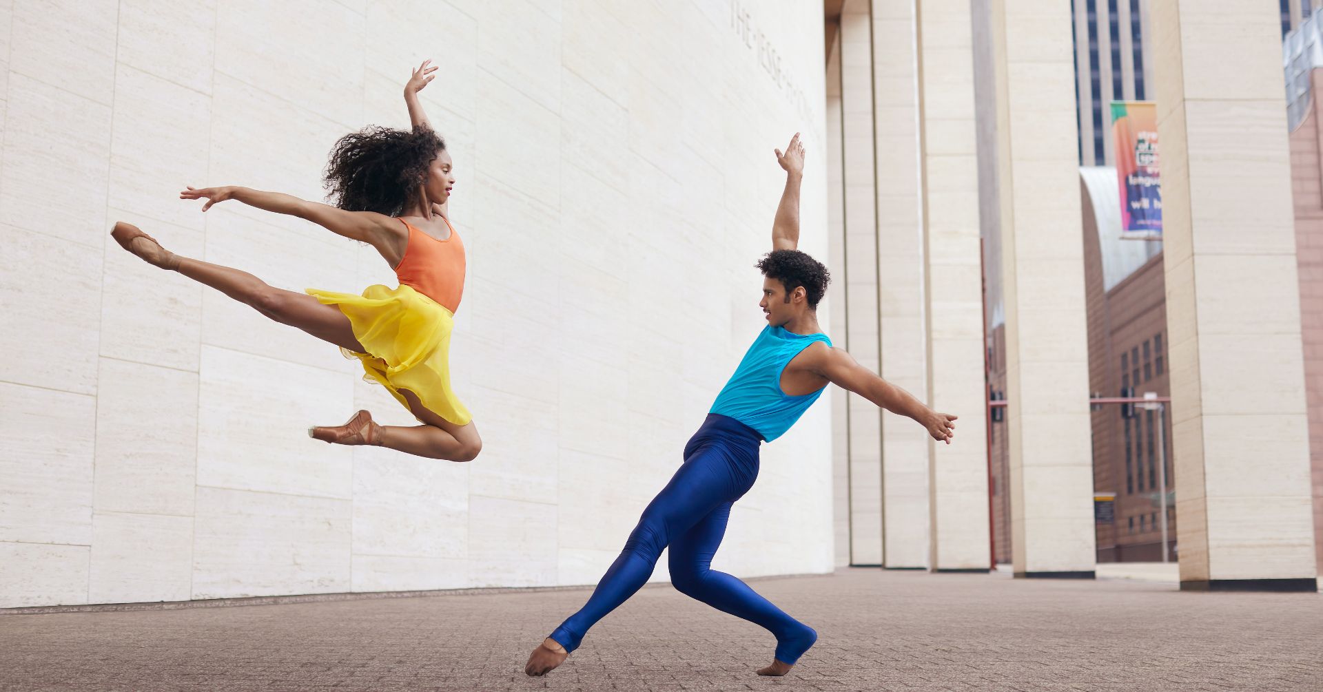 Two dancers on the street. Female dancer is off the ground leaping towards the male dancer.